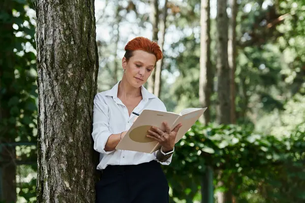 A woman leans against a tree, lost in thought as she writes in a notebook. — Stock Photo