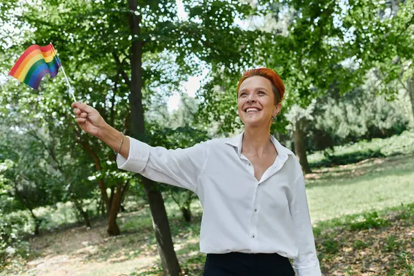A teacher walks through a campus grove, holding a rainbow flag. — Stock Photo