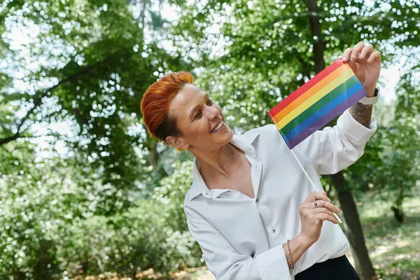 A teacher smiles and holds a rainbow flag in a campus setting. — Stock Photo