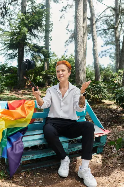 A woman sits on a bench, holding a selfie stick and smiling at the camera. — Stock Photo