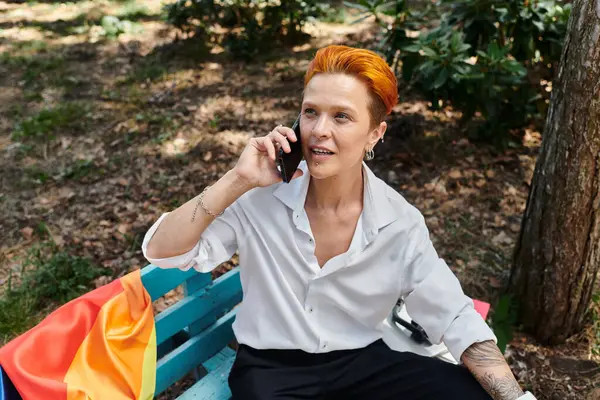 A teacher with red hair sits on a bench on a campus, talking on the phone. — Stock Photo
