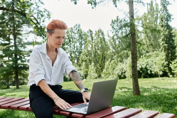 A teacher sits on a bench, working on a laptop in a lush green campus setting. — Stock Photo