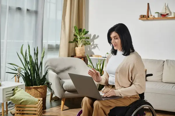A woman in a wheelchair sits in a living room, using a laptop. — Stock Photo