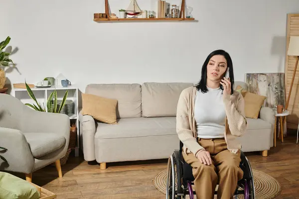 A woman in a wheelchair uses her phone while sitting in a living room. — Stock Photo