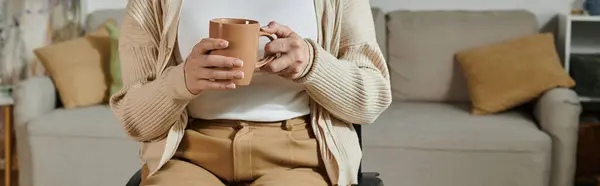 A woman in a wheelchair sits comfortably in her living room, holding a warm mug. — Stock Photo
