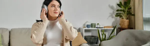 Une femme en fauteuil roulant se détend sur un canapé, écoutant de la musique à travers des écouteurs. — Photo de stock