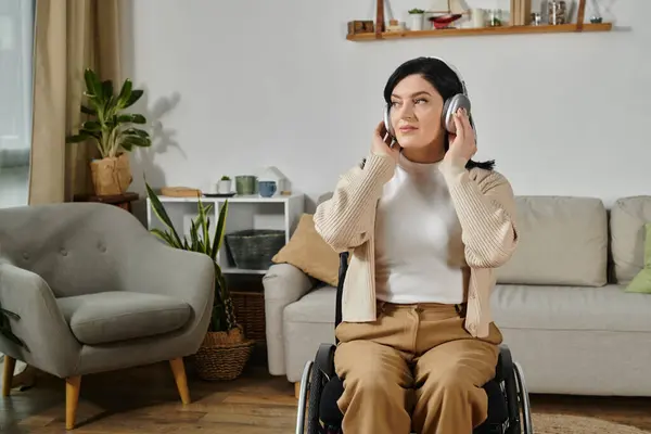 A woman in a wheelchair listens to music with headphones in her living room. — Stock Photo