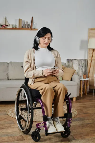 A woman sits in a wheelchair, listening to music on her headphones while holding her phone. — Stock Photo