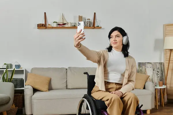 A woman in a wheelchair smiles as she takes a selfie in a comfortable living room setting. — Stock Photo