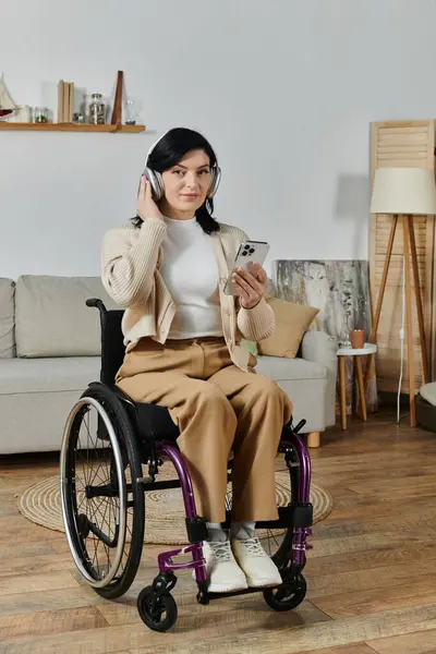 A woman in a wheelchair listens to music on her smartphone with headphones. — Stock Photo