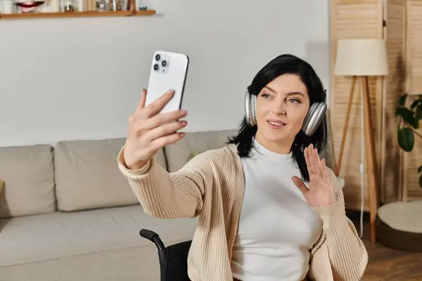 A woman in a wheelchair smiles and waves while video chatting on her phone. — Stock Photo