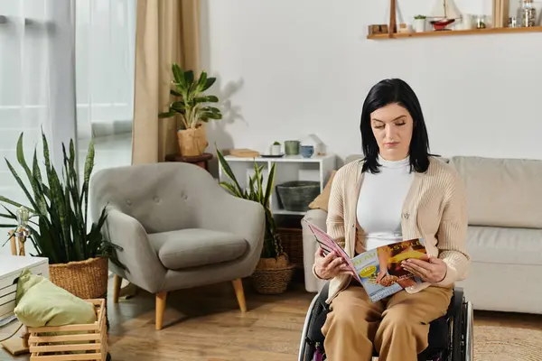 Una mujer en silla de ruedas se sienta en una sala de estar, leyendo una revista. - foto de stock