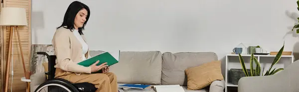 A woman sits in a wheelchair, reading a book in a brightly lit living room. — Stock Photo