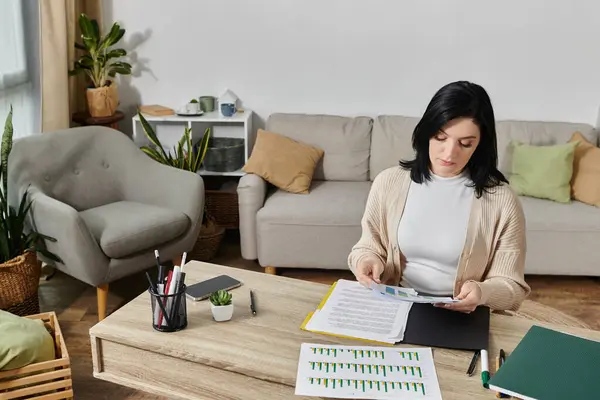 A woman in a wheelchair works at a desk in her home, reviewing documents and charts. — Stock Photo