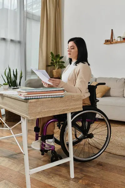 Una donna su una sedia a rotelle si siede a una scrivania, leggendo documenti. — Foto stock