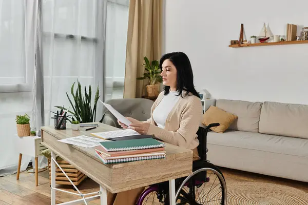 A woman in a wheelchair sits at a desk, reading documents. — Stock Photo