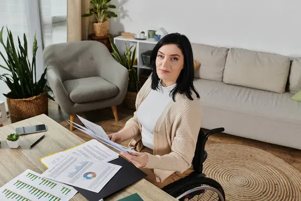 Une femme en fauteuil roulant travaille à un bureau dans sa maison, examinant les documents. — Photo de stock
