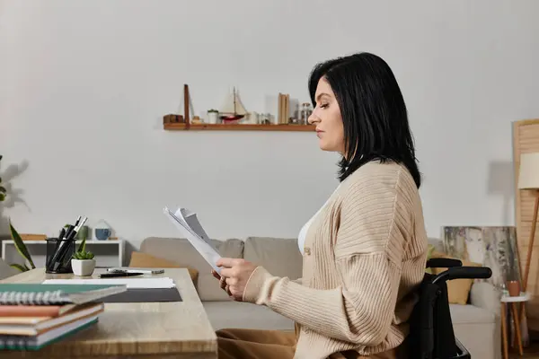 Una donna si siede su una sedia a rotelle a una scrivania, leggendo alcuni giornali. — Foto stock