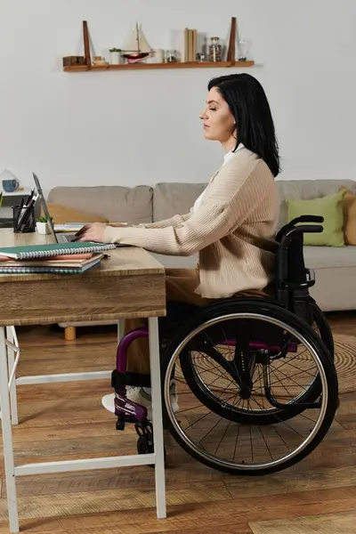 A woman in a wheelchair works on her laptop at a desk in her home. — Stock Photo
