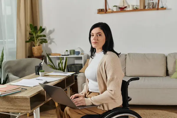 A woman sits in a wheelchair, working on a laptop at a desk in her home. — Stock Photo