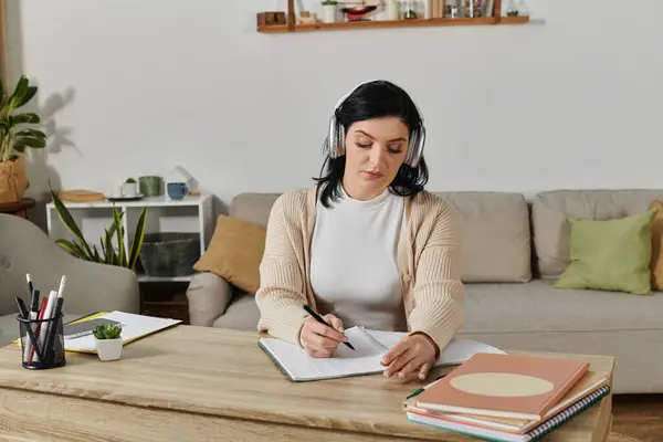 A woman in a wheelchair is sitting at a table, wearing headphones and taking notes. — Stock Photo