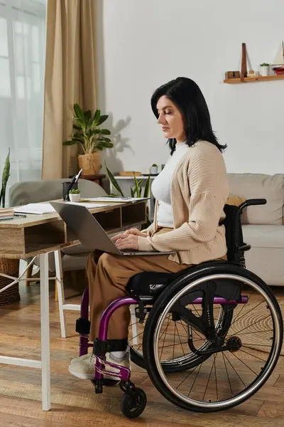 A woman sits in a wheelchair at a desk, using a laptop. — Stock Photo
