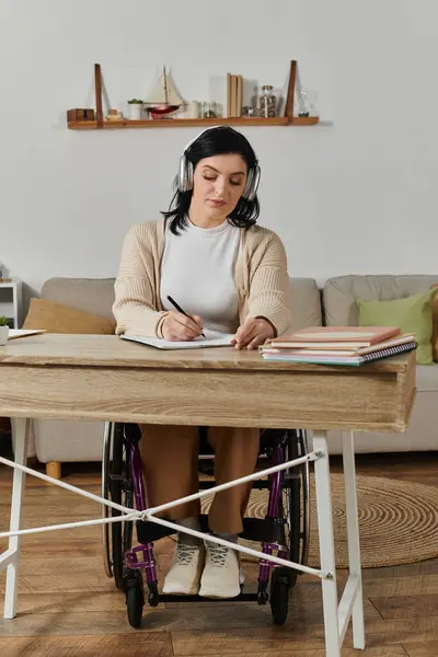 A woman in a wheelchair sits at a desk, writing in a notebook. — Stock Photo