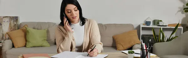 A woman in a wheelchair makes a phone call while sitting on a couch and writing in a notebook. — Stock Photo