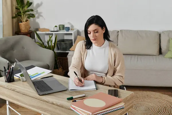 A woman in a wheelchair sits at a desk, focused on writing in a notebook. — Stock Photo