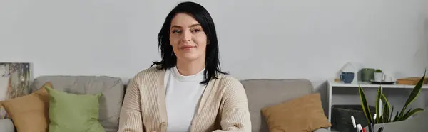 Женщина с темными волосами улыбается, сидя на диване в гостиной. — стоковое фото