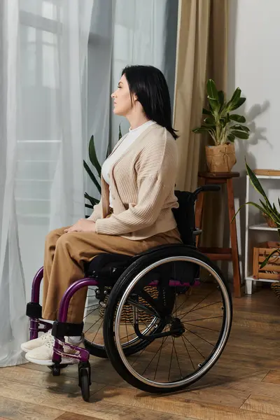 A woman sits in a wheelchair, facing a window, with her gaze directed towards the view outside. — Stock Photo