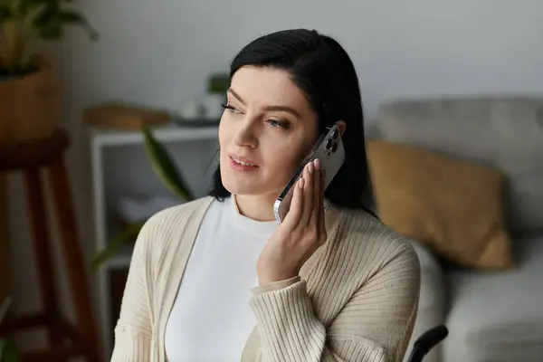 Una donna sulla sedia a rotelle parla al telefono mentre è seduta in un accogliente soggiorno. — Foto stock