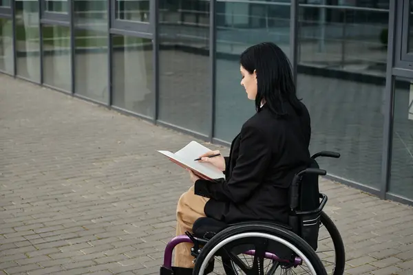 A woman in a wheelchair is seated outside, writing in a notebook. — Stock Photo