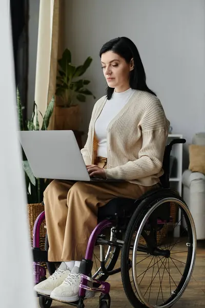 A woman in a wheelchair uses her laptop while sitting in a home. — Stock Photo