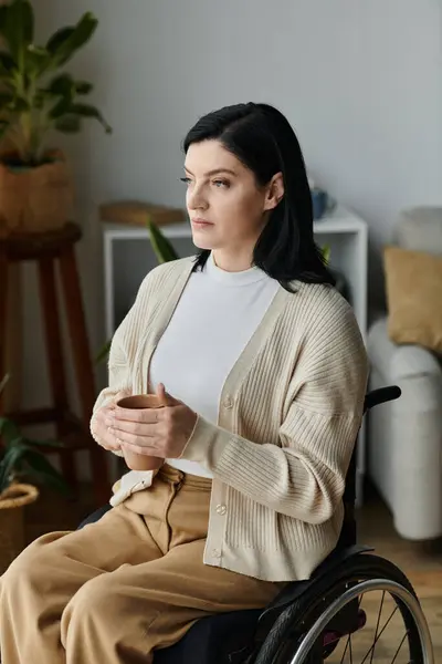 A woman in a wheelchair holds a cup of tea and looks out a window. — Stock Photo