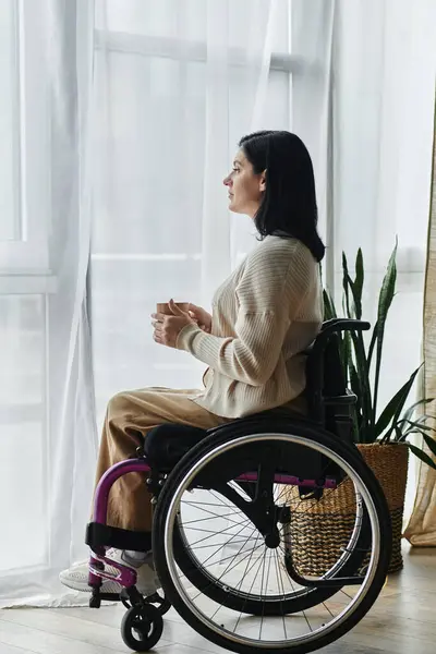 A woman in a wheelchair sits by a window, lost in thought. — Stock Photo