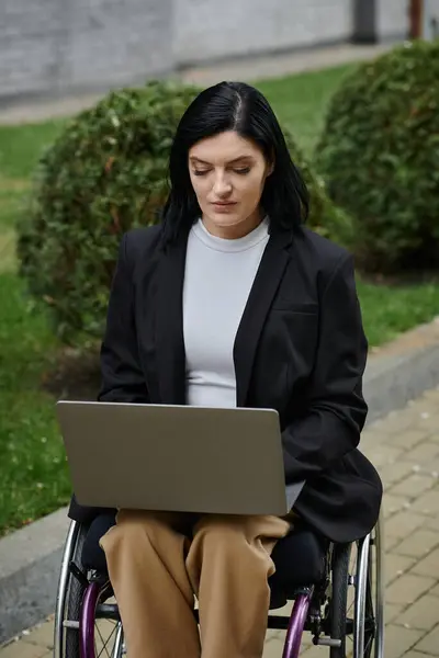 Woman in wheelchair with long black hair using laptop in park — Stock Photo