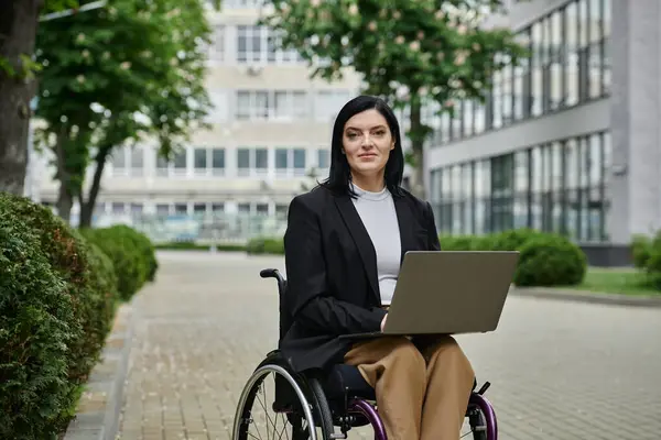 A woman in a wheelchair looks directly at the camera while holding a laptop in her lap. — Stock Photo