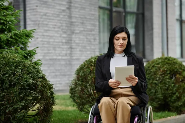 A woman in a wheelchair uses a tablet outside, focusing intently on the screen. — Stock Photo
