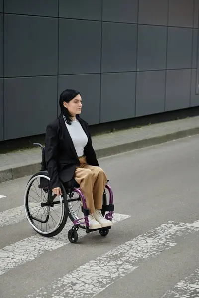 A woman in a wheelchair crosses a street in front of a building. — Stock Photo