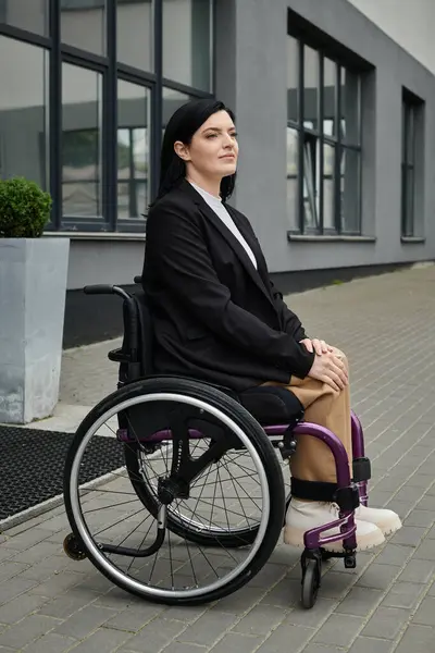 A woman in a wheelchair sits outside a building, looking upwards. — Stock Photo