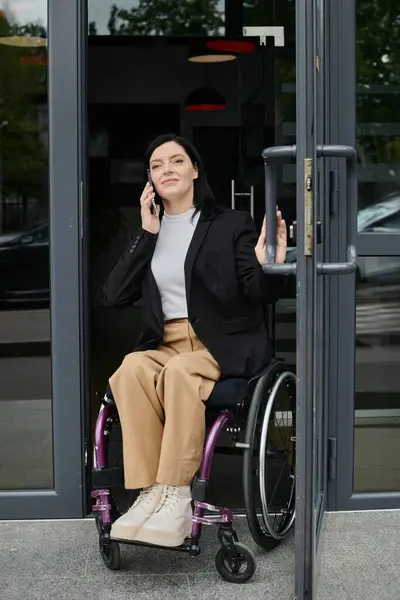 A woman in a wheelchair is entering a building while speaking on the phone. — Stock Photo