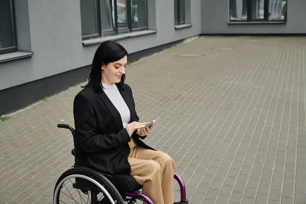 Una mujer en silla de ruedas sonríe mientras usa su teléfono en una calle de la ciudad. — Stock Photo