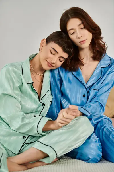 Due donne in pigiama, una con la testa appoggiata sulla spalla dell'altra, si guardano amorevolmente. — Foto stock