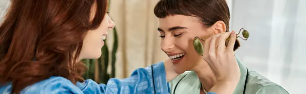 A young couple in pajamas relaxes on a bright morning, enjoying a playful moment with a jade roller. — Stock Photo