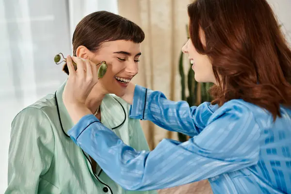 Ein junges lesbisches Paar genießt einen entspannten Morgen zusammen, wobei eines auf der anderen Seite eine Jade-Rolle benutzt. — Stockfoto