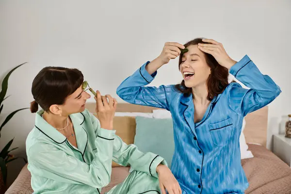 A young lesbian couple, wearing pajamas, relaxes on a bed as they enjoy a morning skincare routine together. — Stock Photo