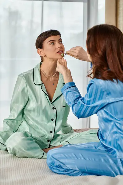 A young lesbian couple in their pajamas relax on a bed, enjoying a quiet morning together. — Stock Photo