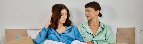 A young lesbian couple relaxes in bed, wearing pajamas, enjoying a moment of closeness. — Stock Photo