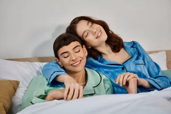 Ein junges lesbisches Paar entspannt im Bett, trägt Schlafanzug und genießt einen Moment der Nähe und Verbundenheit. — Stockfoto